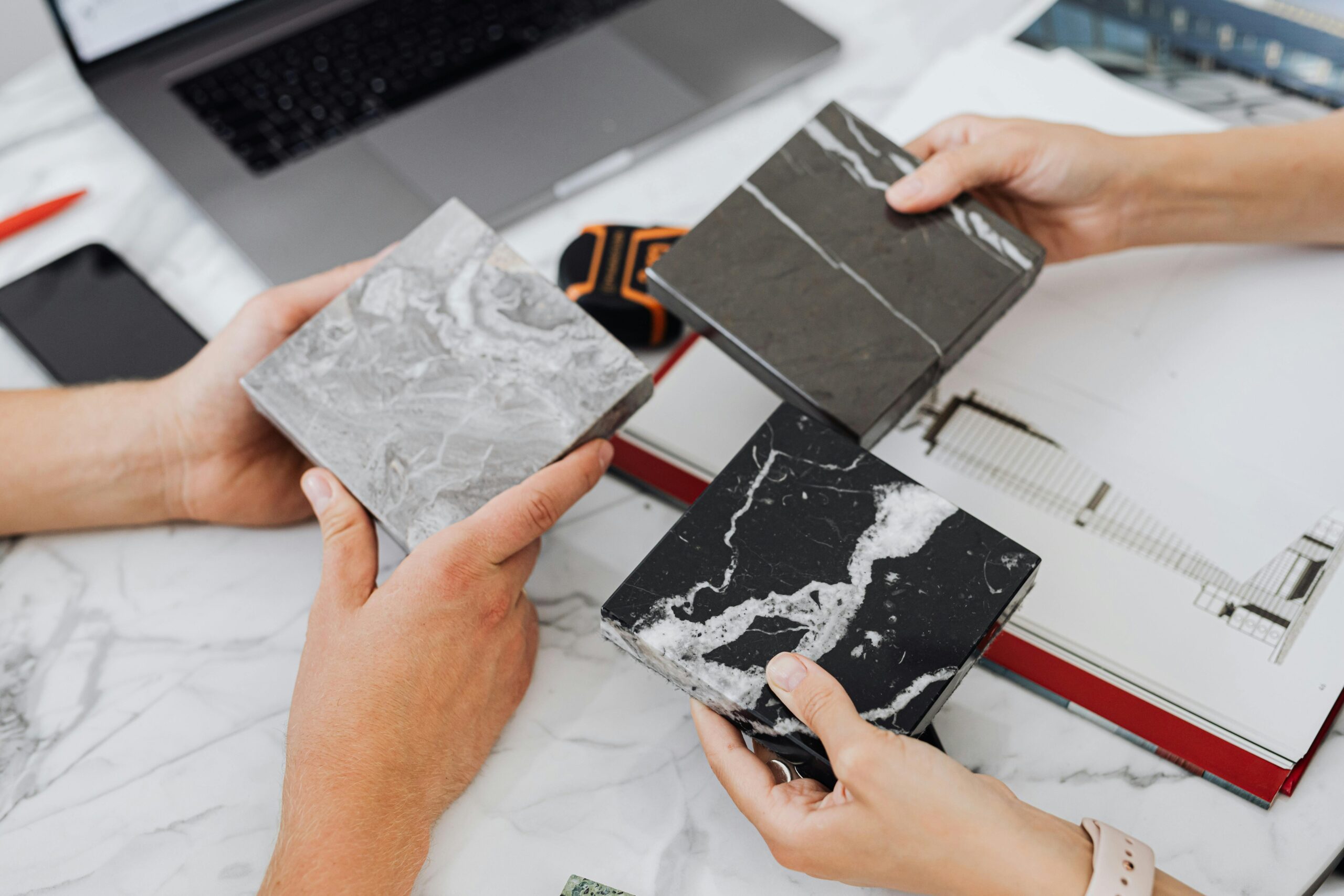 Two architects selecting marble tile samples on a desk in an office setting.